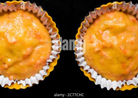 The process of making carrot muffins. Dough for cakes in paper molds on a black background. Selective focus, top view. Stock Photo