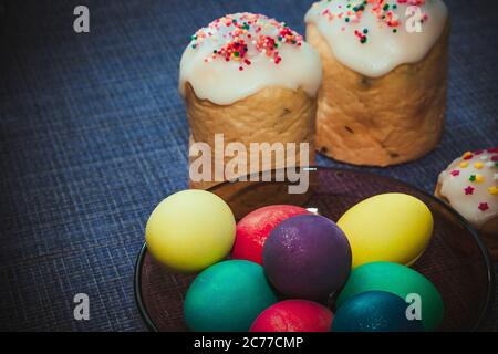 Many small cakes in the glaze for the holiday Easter. Colored eggs on a dark blue background Stock Photo