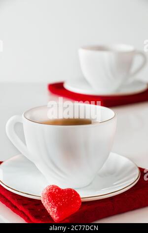 Two white cups of tea on a white background. Heart shaped marmalade, symbol of Valentine's Day and love. The concept of a meeting of two lovers. Stock Photo