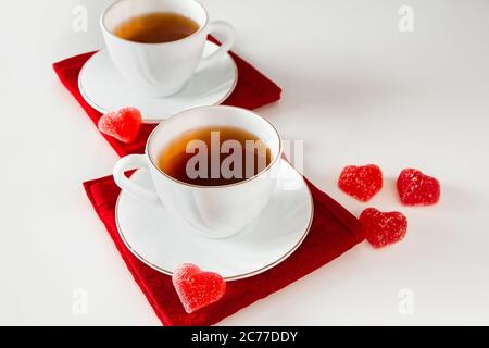 Two white cups of tea on a white background. Heart shaped marmalade, symbol of Valentine's Day and love. The concept of a meeting of two lovers. Stock Photo
