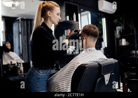 Portrait of a man in Barbershop, shave and cut by barber girl