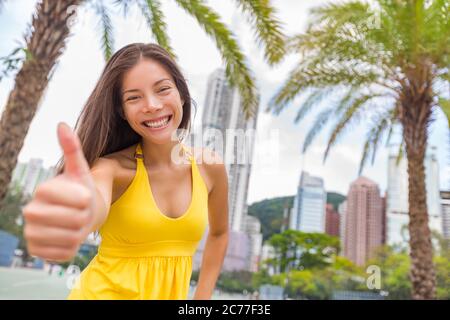 Happy chinese girl doing thumbs up in satisfaction in Hong Kong city, Asia China travel lifestyle. Young smiling multiracial woman Stock Photo
