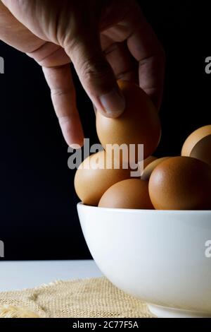 Close up fresh chicken eggs on linen tablecloth and white table with copy space .Hand man hold chicken egg. Stock Photo