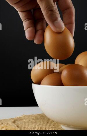 Close up fresh chicken eggs on linen tablecloth and white table with copy space .Hand man hold chicken egg. Stock Photo