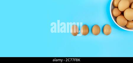 Top view Fresh chicken eggs in white bowl and chicken eggs on blue background with copy space. Uncooked raw eggs in bowl isolated banner. Stock Photo
