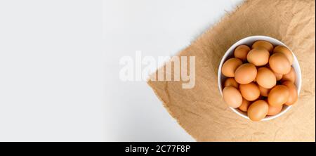 Top view Fresh chicken eggs in white bowl on white color wooden table with copy space. Uncooked raw eggs in bowl on table banner. Stock Photo