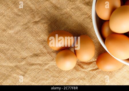 Top view fresh chicken eggs and blur fresh chicken eggs in white bowl on linen tablecloth with copy space. Uncooked raw eggs in bowl. Stock Photo