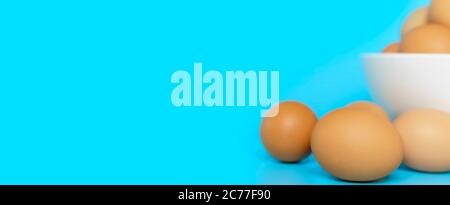 Close up Fresh chicken eggs with blur chicken eggs in white bowl  on blue background with copy space. Uncooked raw eggs  isolated banner. Stock Photo