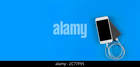 Top view smartphone charging with power bank on blue background with copy space. Smartphone charging with power bank by white USB cable. Stock Photo