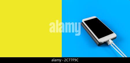 Top view smartphone charging with power bank on blue and empty yellow background with copy space. Smartphone charging with power bank by white USB cab Stock Photo