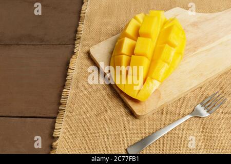 Yellow half  mango with small fork. Mango fruit cubes on the wooden table. Tropical fruit asia. Fresh yellow mango peel and Sliced cubes on wood butch Stock Photo