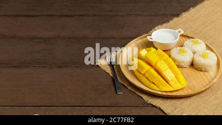 Yellow half  mango with small fork. Mango fruit cubes on the wooden table. Tropical fruit asia. Fresh yellow mango peel and Sliced cubes on wood butch Stock Photo