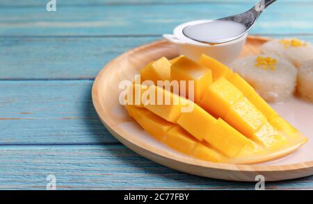 Close up Fresh yellow mango peel and Sliced cubes with sticky rice. Spoon pouring coconut milk on top mango. Favorite thai dessert summer. Mango on wo Stock Photo