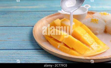 Close up Fresh yellow mango peel and Sliced cubes with sticky rice. Spoon pouring coconut milk on top mango. Favorite thai dessert summer. Mango on wo Stock Photo