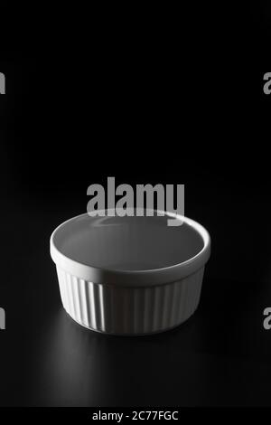 Empty white Ramekin on black background with copy space. Stock Photo