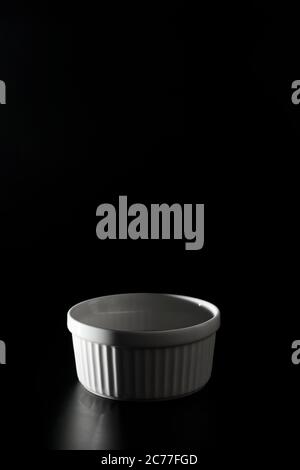 Empty white Ramekin on black background with copy space. Stock Photo