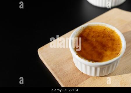 Close up homemade creme brulee in white ramekin  with sugar burn top up on black background with copy space. French dessert creme brulee Stock Photo
