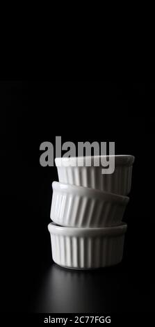 White ramekins stacked on black background with copy space. Stock Photo