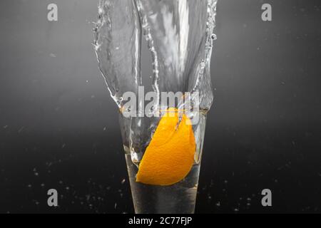 Orange slice falling and dropping into a splashing glass with black background. Stock Photo