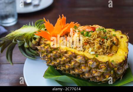 Thai royal pineapple fried rice. Fried rice with shrimps served in a pineapple on wood table. Stock Photo