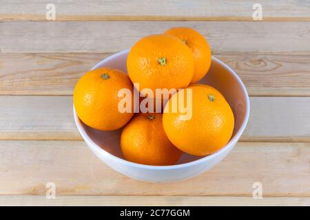 Fresh oranges in white bowl on wood table. Stock Photo