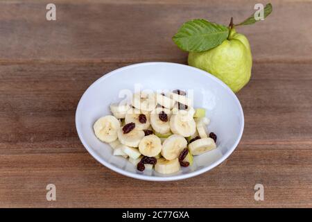 healthy food banana slide guava block and raisins in white bowl on wood table. With copy space for text or design. Stock Photo