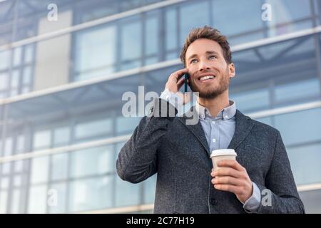 Man talking on smartphone. Businessman urban professional business man using mobile phone smiling drinking coffee at office building in city. Happy Stock Photo