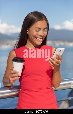 Happy Asian business woman on coffee break smiling texting sms message mobile data phone or reading online. City urban businesspeople lifestyle Stock Photo