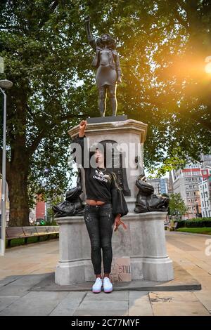 Jen Reid poses in front of her black resin and steel statue titled A Surge of Power (Jen Reid) 2020, by Marc Quinn, where it is installed on the vacant Edward Colston plinth in Bristol city centre. Stock Photo