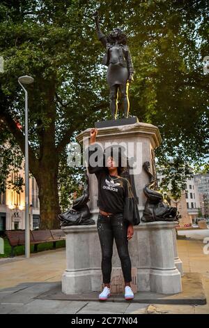Jen Reid poses in front of her black resin and steel statue titled A Surge of Power (Jen Reid) 2020, by Marc Quinn, where it is installed on the vacant Edward Colston plinth in Bristol city centre. Stock Photo