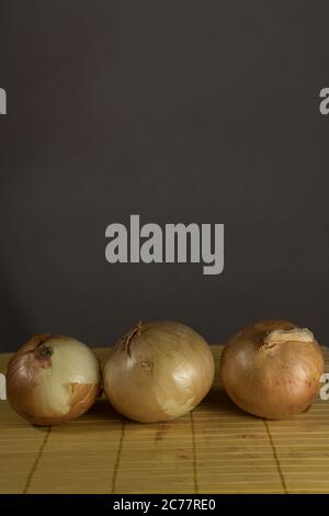 Three onions on board cutting, brown background Stock Photo