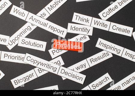 Cut paper inscription priorities on a red background, surrounded by other inscriptions on a dark background. Word cloud concept Stock Photo