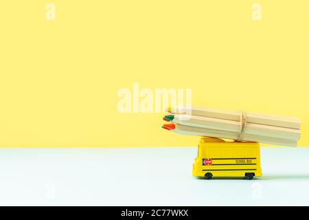 Back to school composition with yellow school bus model and wooden colour pencils on pink background. Transport for students. With space for text Stock Photo