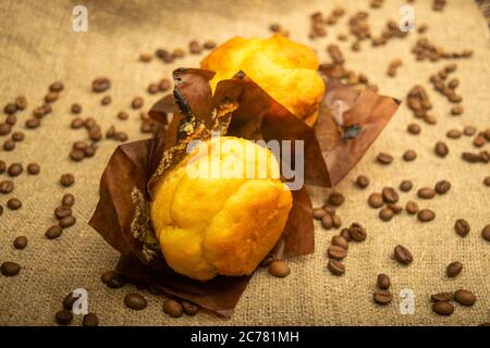 Two fresh cupcakes and coffee beans on a rough-textured homespun fabric. Close up Stock Photo