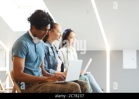 Side view of concentrated multi-ethnic students sitting in row and using laptops for notes at lecture Stock Photo