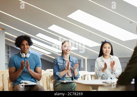 Cheerful young multi-ethnic students sitting in row and applauding professor after interesting lecture Stock Photo