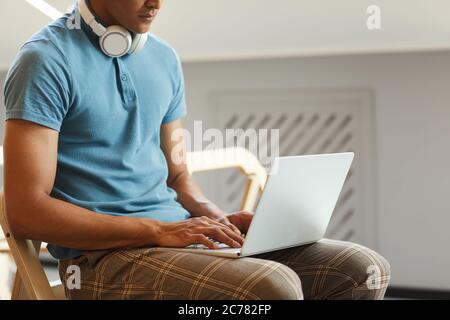 Close-up of serious mixed race student guy sitting on chair and using laptop while searching for information on internet Stock Photo
