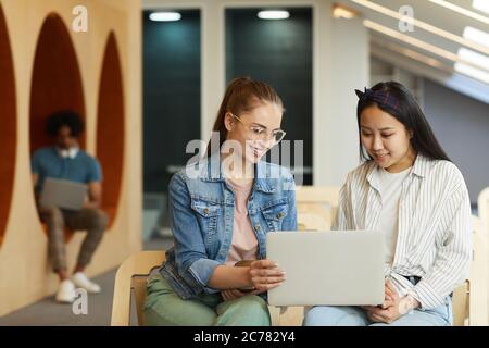 Content multi-ethnic students sitting in modern hall and working on university project together using laptop Stock Photo