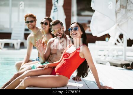 Young people sitting near the swimming pool sunbathing and smiling Stock Photo