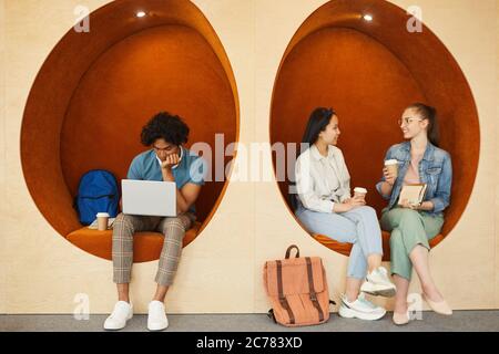 Modern multi-ethnic students sitting in comfortable wall chairs and resting during break at university Stock Photo