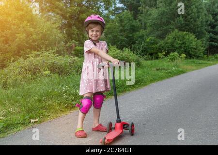 Portrait of active little toddler girl riding scooter on a village road outdoors on summer day. Seasonal child activity sport. Healthy childhood lifes Stock Photo