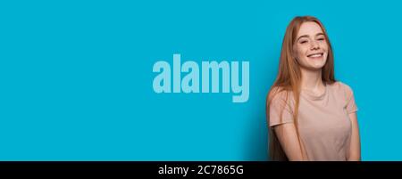 Charming young student with red hair and freckles smiling at camera on blue studio wall with free space Stock Photo