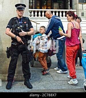 A young boy admiring an armed anti-terrorist policeman standing guard outside Liverpool Street station in London, England, U.K. Stock Photo