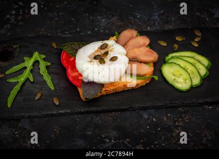 Toast with poached egg and pumpkin seeds, smoked pink salmon slices, tomato, arugula and basil leaves. Healthy meal for breakfast. Stock Photo