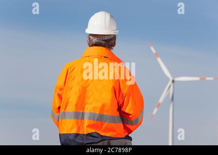 Worker or engineer with hard hat and protecive clothing looking at a windmill of a windfarm - focus on the man Stock Photo