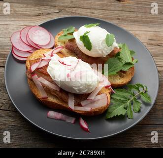 two sandwiches on a toasted white slice of bread with poached eggs, green leaves of arugula and radish in a round plate, top view Stock Photo