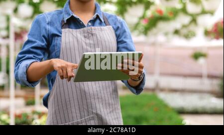 Farm worker and climate control in greenhouse. African american girl works on digital tablet Stock Photo