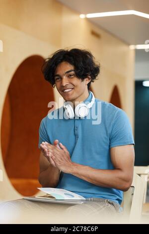 Positive handsome mixed race student with wireless headphones around neck clapping hands while admiring university teacher Stock Photo