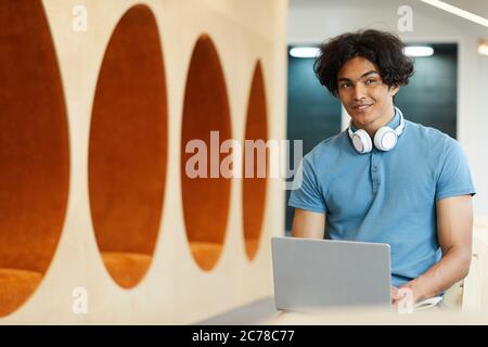 Smiling mixed race student with messy hair sitting in auditorium and typing lecture note on laptop Stock Photo