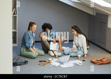 Group of interracial students studying economics students brainstorming about project together using laptop and charts Stock Photo